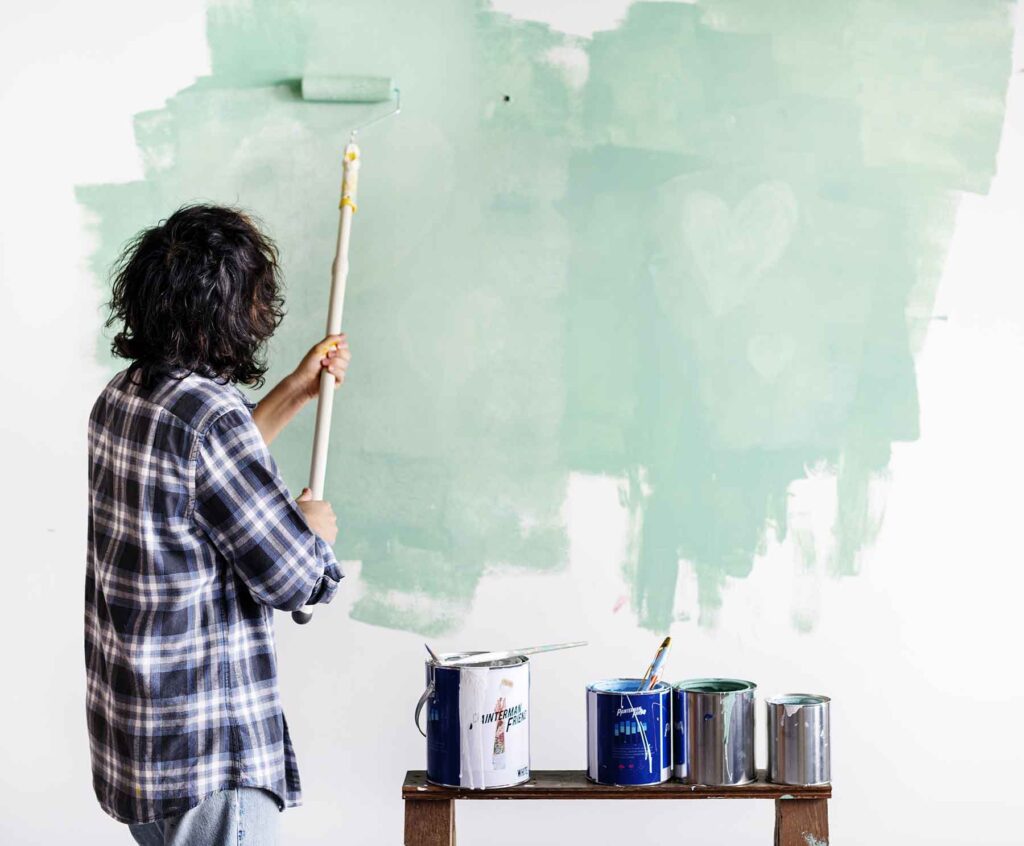 A person paints a wall light green, showing McCandless Plumbing & Excavation can help with home upgrades and inspections.