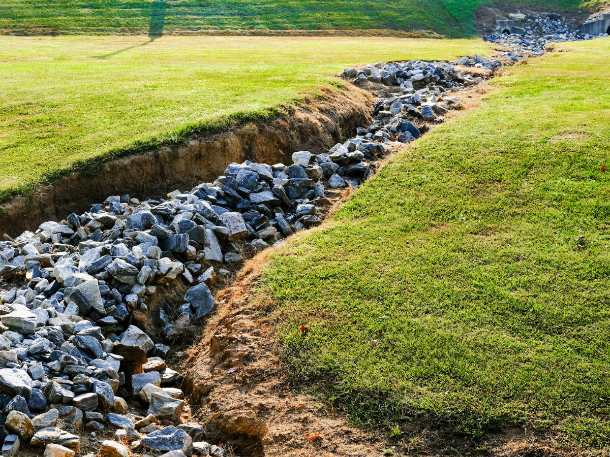 McCandless Plumbing & Excavation shows a safe, well-built drainage ditch made for proper water flow through a grassy area.