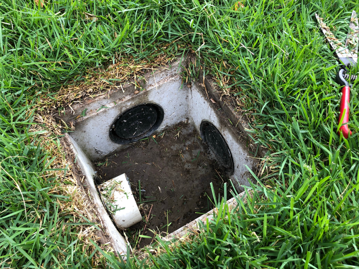 McCandless Plumbing & Excavation shows an open valve box for easy pipe access, ready for septic work using nearby pliers.
