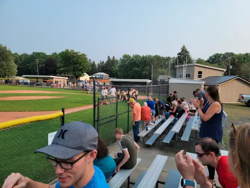 Fans watch a baseball game near a fence with a McCandless Plumbing & Excavation sewer repair sign in the background.