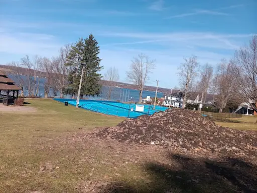 McCandless Plumbing & Excavation is doing outdoor work near a pool, with dirt piled on grass next to water and nearby buildings.