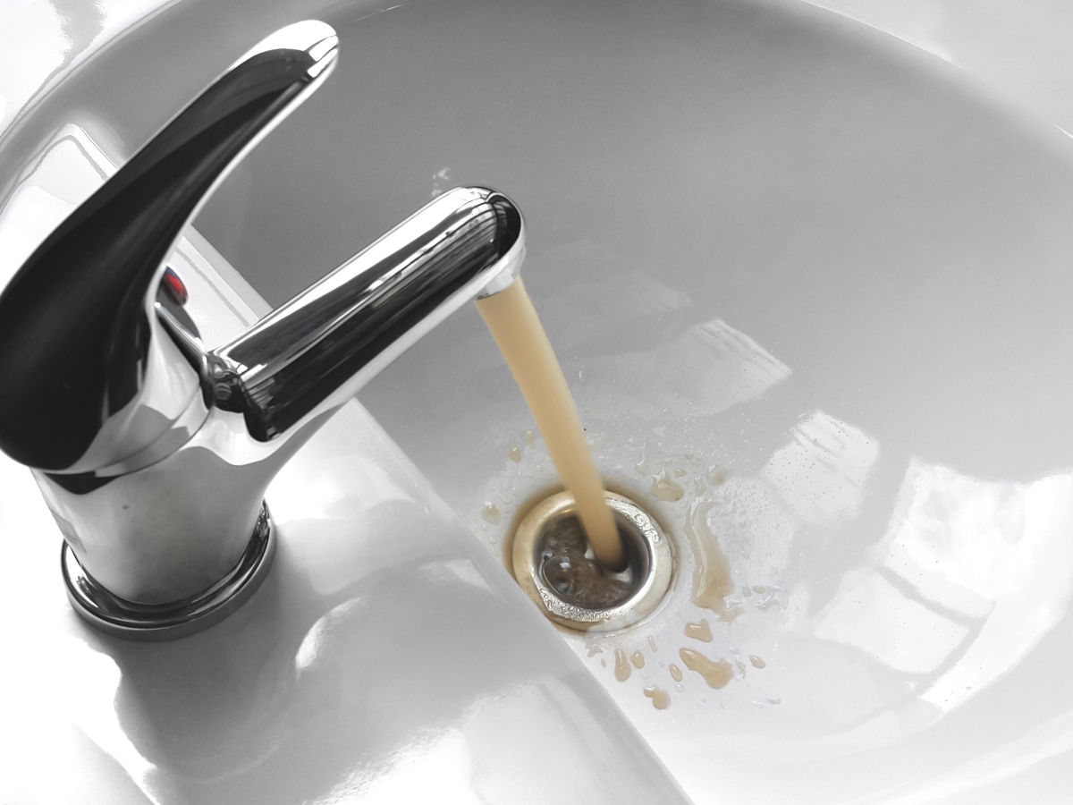 Brown water flows from a faucet, showing a possible plumbing or septic issue fixed by McCandless Plumbing & Excavation.