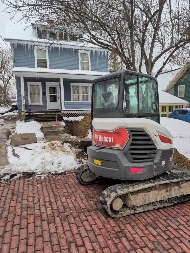 McCandless Plumbing & Excavation working on a home project in winter, showing equipment and supplies by a residential house.