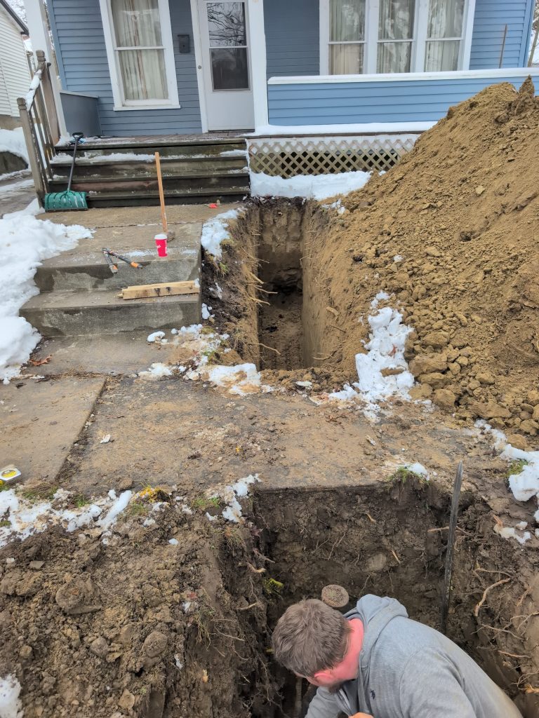 McCandless Plumbing & Excavation works outside a home on a snowy day, repairing pipes in front of the porch.