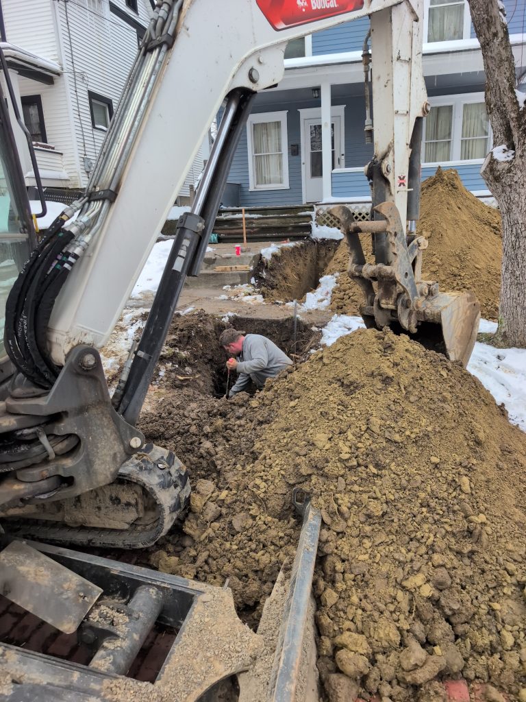 McCandless Plumbing & Excavation works outside a house, digging and making repairs in winter with their equipment.