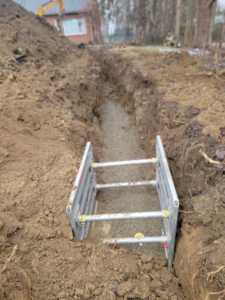 McCandless Plumbing & Excavation prepares a trench safely by using metal supports and proper equipment near a residential area.