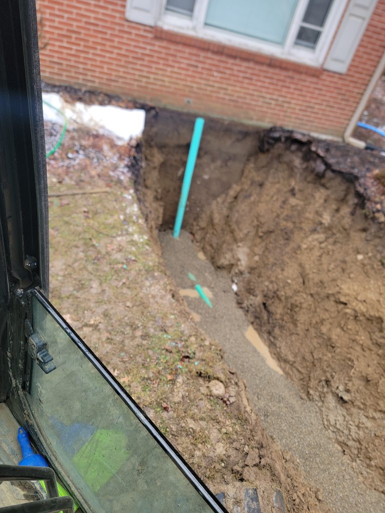 McCandless Plumbing & Excavation is installing a new pipe next to a house, preparing the site for better plumbing.