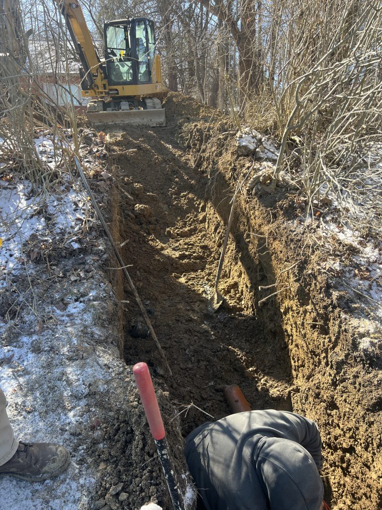 McCandless Plumbing & Excavation worker repairs pipes in a trench, showing expert pipe service even in challenging outdoor conditions.