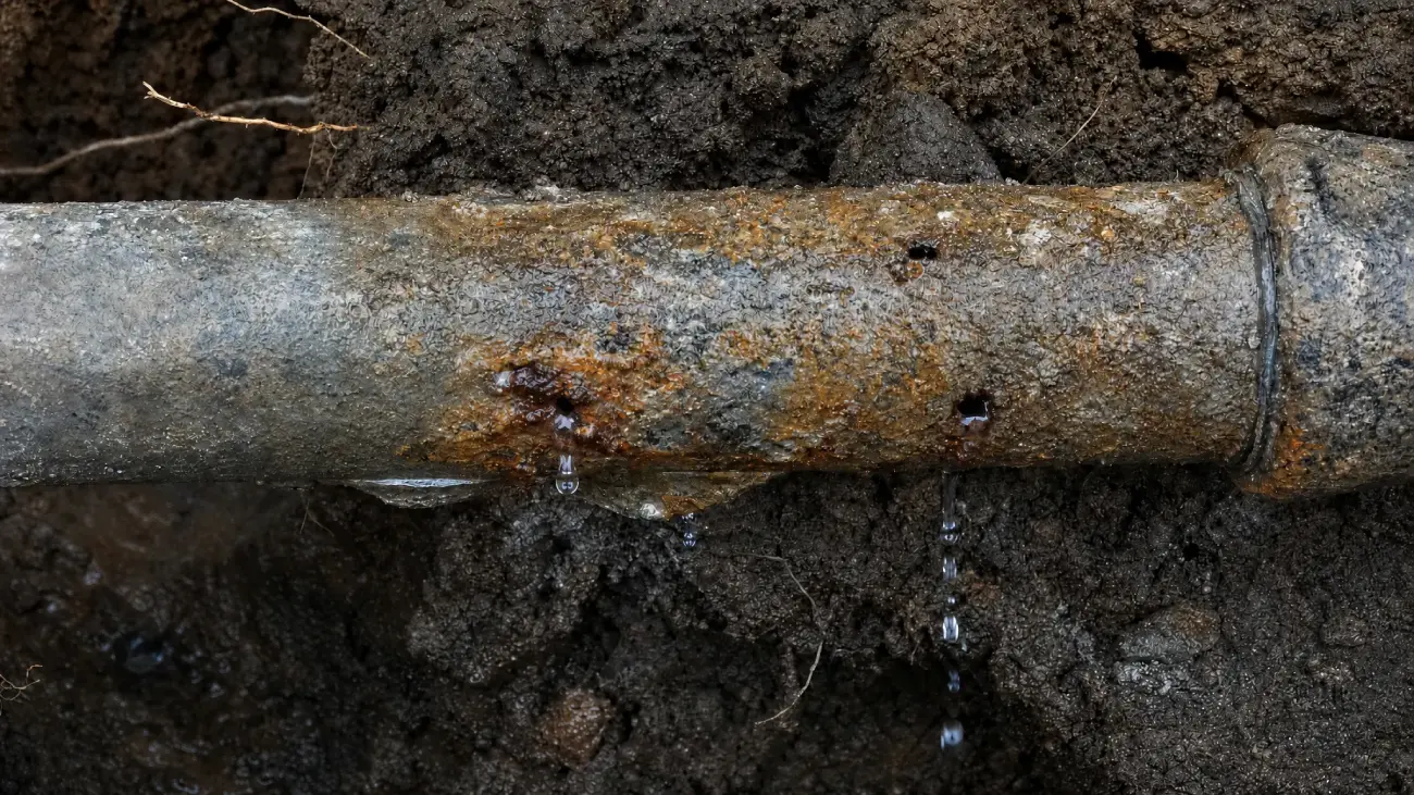 Leaking metal pipe showing need for repair by McCandless Plumbing & Excavation. Water drips onto wet ground.